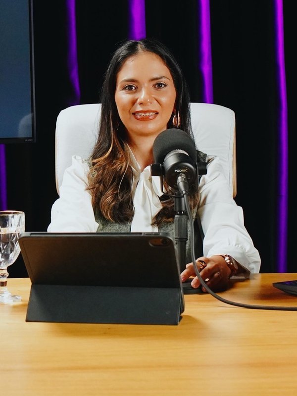 Gicelli Paixão sentada à mesa de um estúdio de gravação, com microfone e tablet à frente